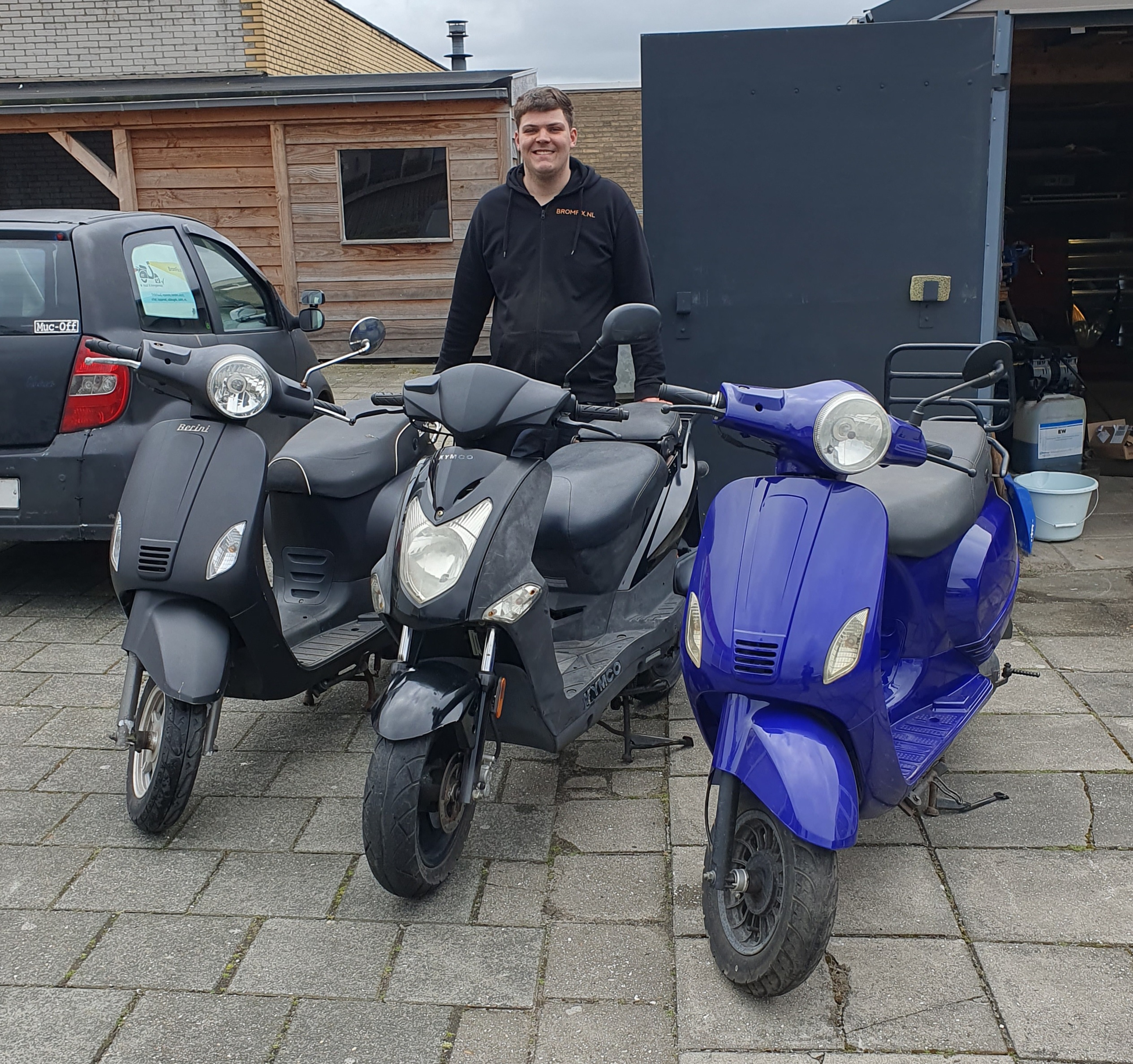 Scooter monteur Roland van Bromfix glimlachend bij drie gebruikte scooters voor zijn werkplaats in Berkel en Rodenrijs, dé expert voor fatbike en scooter reparatie in de regio Rotterdam-Noord, Schiebroek en Hillegersberg.