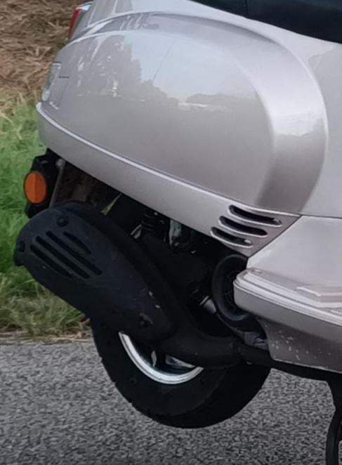 Afbeelding van de nieuwe uitlaat van een scooter, gemonteerd op de rechter achterzijde van een beige model. Laat de zwarte hitteschildbescherming zien. Geschikt als voorbeeld voor mensen die zoeken naar 'nieuwe uitlaat scooter' of 'scooter uitlaat kapot'. Gemonteerd door Roland van Bromfix.